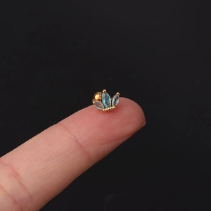 Macro shot of gold crown stud earring with marquise blue zircon held on fingertip