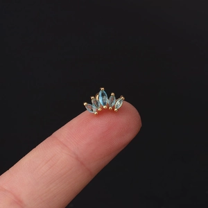 Close-up of golden crown stud earring with light blue marquise zircon on a fingertip