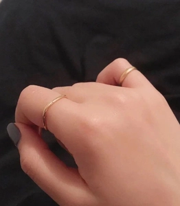 Close-up of two minimalist gold square rings worn on hand over a black background