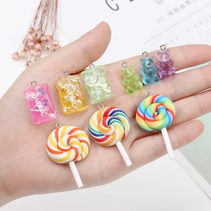 Macro detail of colorful resin gummy bear and lollipop charms held in hand for DIY jewelry