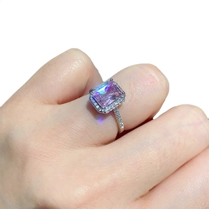 Pink rectangular halo ring with sparkling side stones shown on a finger