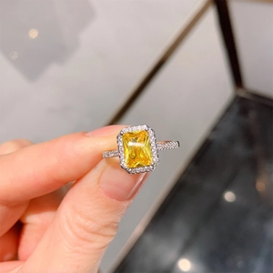 Radiant cut yellow gemstone ring with diamond halo and pave band on a finger