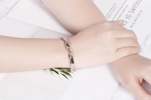 Close-up of a silver twisted open C-shape bracelet worn on a wrist with fuzzy background
