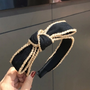 Cerchietto elegante in tessuto nero con grande fiocco e bordo a catena dorata