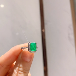 Macro detail of emerald cut green gemstone ring with halo diamonds on silver band