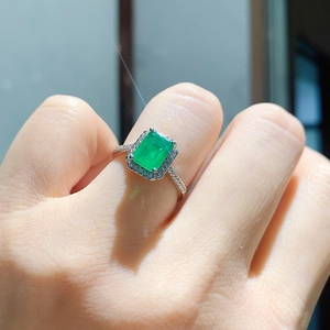 Close-up of square cut emerald green gemstone ring in silver halo setting on finger