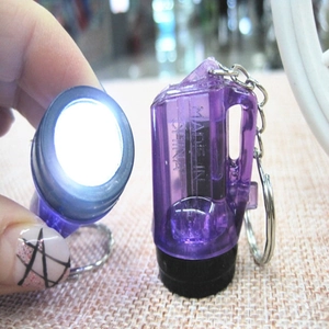 Close-up of hand holding a mini purple LED flashlight keychain emitting bright light