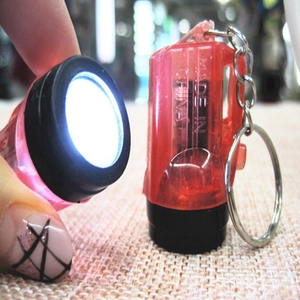 Mini LED keychain flashlight in red transparent plastic with metal ring on hand