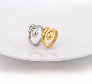 Close-up of polished steel and gold geometric waterdrop rings on a white plate