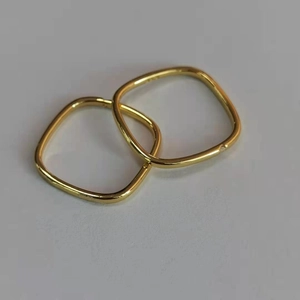 Close-up of two interlocking gold geometric square rings on a neutral gray surface