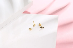 Detail of gold rhombus stud earrings with star engraving on white geometric stands