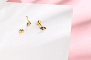 Detail of gold rhombus stud earrings with black enamel starburst and screw backs
