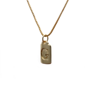 Macro detail of gold-plated copper rectangle pendant with engraved letter G on a fine chain
