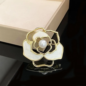 Macro detail of camellia brooch with white enamel petals and central pearl on black surface