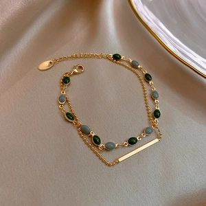 Détail d'un bracelet doré double couche avec perles ovales vertes et grises sur soie