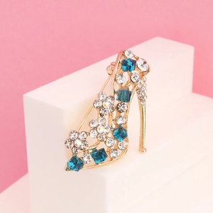 Elegant gold high heel brooch with blue and clear rhinestones on a decorative pedestal