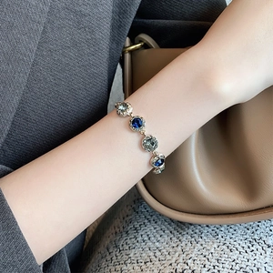 Gold-plated bracelet with blue and grey gemstones on model with leather bag