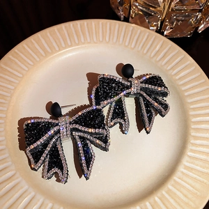 Close-up of elegant black bow earrings with sparkling rhinestones on a beige ceramic plate
