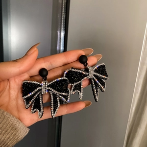 Macro shot of black bow earrings with sparkling rhinestones held by a hand