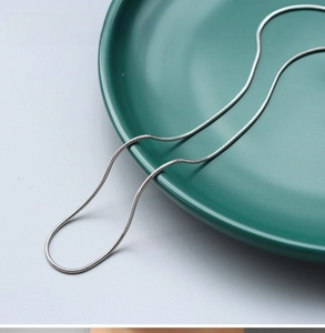 Detail of 1.3mm steel silver round snake chain necklace on a ceramic plate