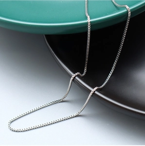 Macro shot of 1.2mm steel box chain necklace resting on a ceramic surface