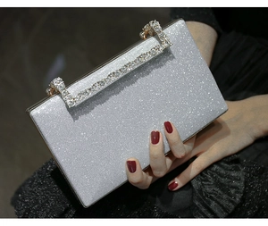 Silver glitter evening clutch bag featuring a sparkling rhinestone handle held by hand