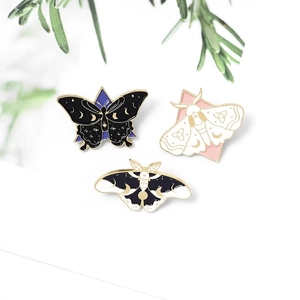 Three enamel pins featuring butterfly and moth designs with moon and stars on a white base