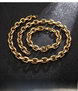 Detail of chunky gold-tone stainless steel cable chain necklace and bracelet set on black background