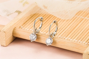 Close-up of S925 silver hoop earrings with a sparkling round diamond drop on bamboo