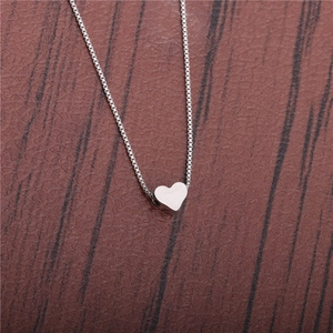 Close-up of a polished silver heart pendant necklace on a brown textured leather surface