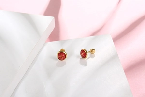 Detailed close-up of vintage gold stud earrings with red cracked stone on a pink background