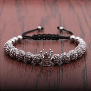 Macro detail of silver crown pendant and zircon spheres on black woven bracelet