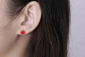Close-up of red apple stud earrings with green leaf detail worn on the earlobe