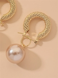 Macro detail of gold twisted C-shape hoop earring featuring a large round pink pearl drop