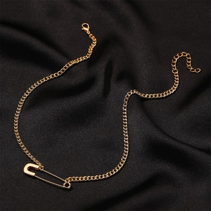 Elegant gold safety pin pendant necklace displayed on a luxury black satin background