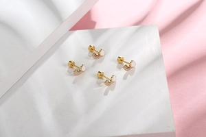 Detailed view of rainbow cloud stud earrings in gold finish on white stone stand