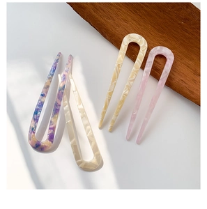 Close-up of four floral acetate U-shaped hair pins on a white background with wood