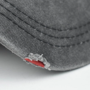 Detail of washed denim baseball cap brim featuring vintage distressed rips and red accents