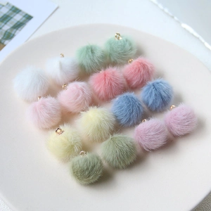 Macro view of assorted colorful plush pompom charms with gold metal loops in a white tray