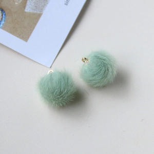 Detail view of two mint green fluffy pompom pendants with golden metal hooks for DIY