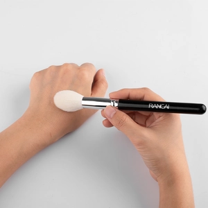 Flame shaped highlighter brush with white soft bristles and black handle shown in action