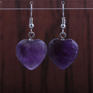 Macro detail of heart-shaped amethyst earrings with silver hooks on dark wood
