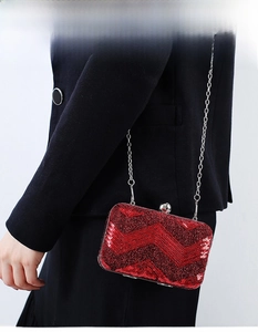 Detail of red sequin evening bag with wavy stripes and silver chain on dark blazer