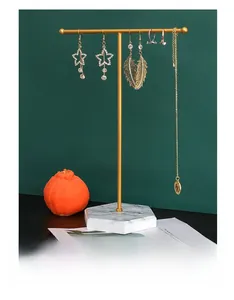 Detail eines goldenen T-Schmuckständers mit weißem Marmorsockel für Ohrringe und Ketten