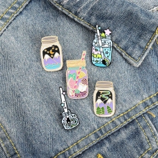 Flat lay of artistic enamel pins with space and fruit glass jar designs on denim cloth