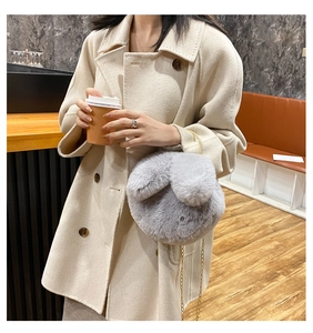 Detail of grey plush rabbit ear bag with gold metal chain on a warm-toned coat