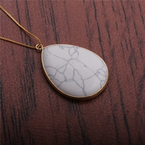 Macro shot of a teardrop-shaped white marble pendant on a delicate gold chain
