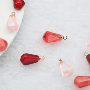 Red and pink pomegranate seed charms with gold metal loops on a white velvet surface