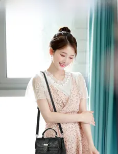 Detail of a black woven crossbody bag held by a model in a floral dress near a window