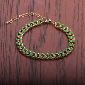 Hip hop style gold Cuban link bracelet with green enamel center on wood background